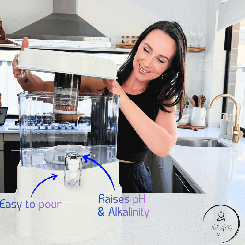 Woman using HolyH₂O™ Trinity Filter in a kitchen, highlighting easy pour and pH raising features.