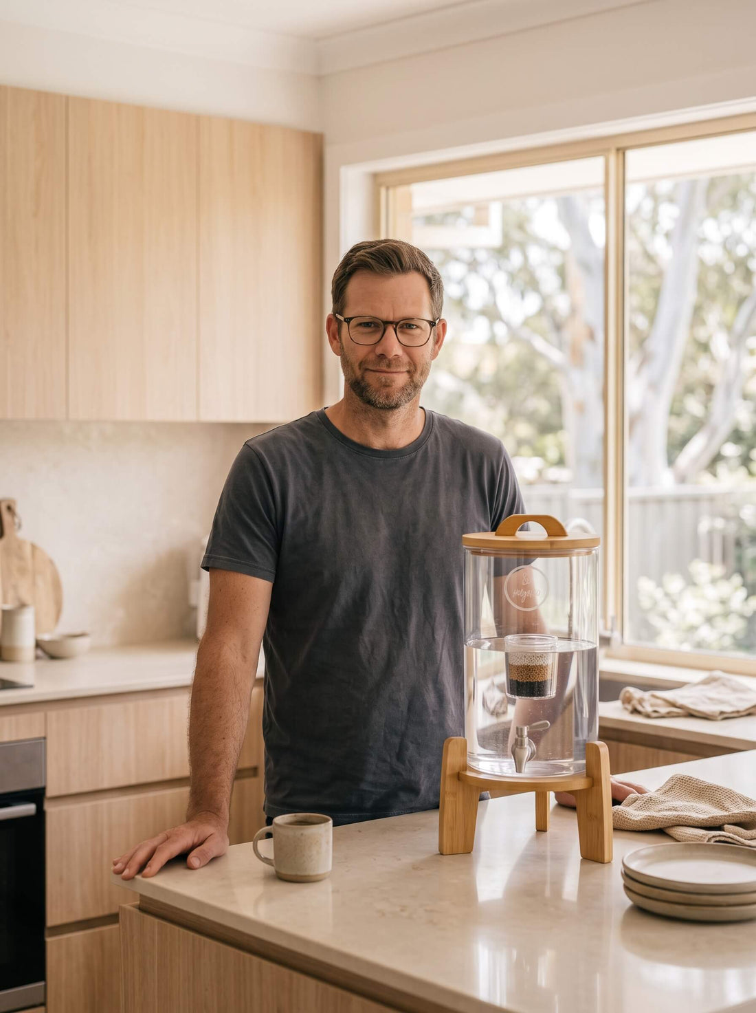 AJ, founder of HolyH₂O, in his Sydney kitchen beside the glass Trinity filter